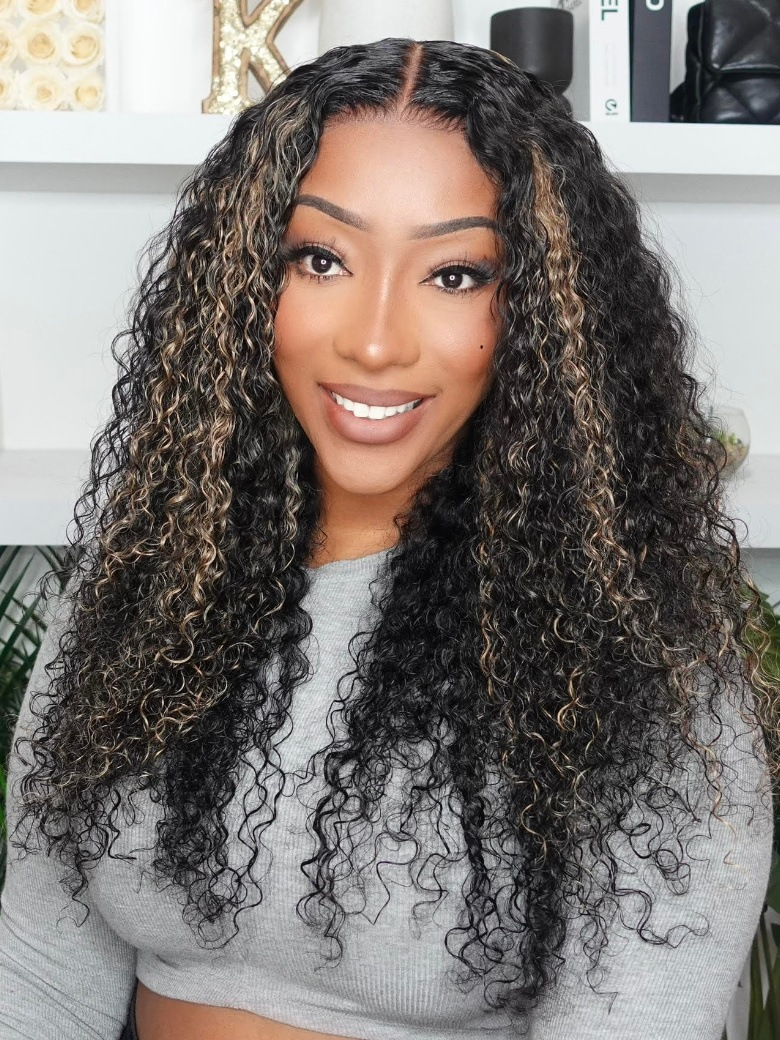 A model displays the UNice 22''=119 Bye Bye Knots Wig 7x5 Glueless Lace Black With Blonde Highlights, showing a model with long curly hair wearing a grey sweater.