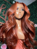 A model displays the UNice Bye Bye Knots 7x5 Lace Loose Wave Red Orange Highlights Wig with Face Framing, showing a wig with long red hair and a rose and loose wave.