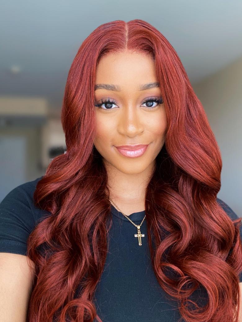 A model displays the UNice Dark Auburn Body Wave Remy Human Hair 4 Bundles With Closure Deal, showing a model with long red hair and a black shirt and body wave texture.
