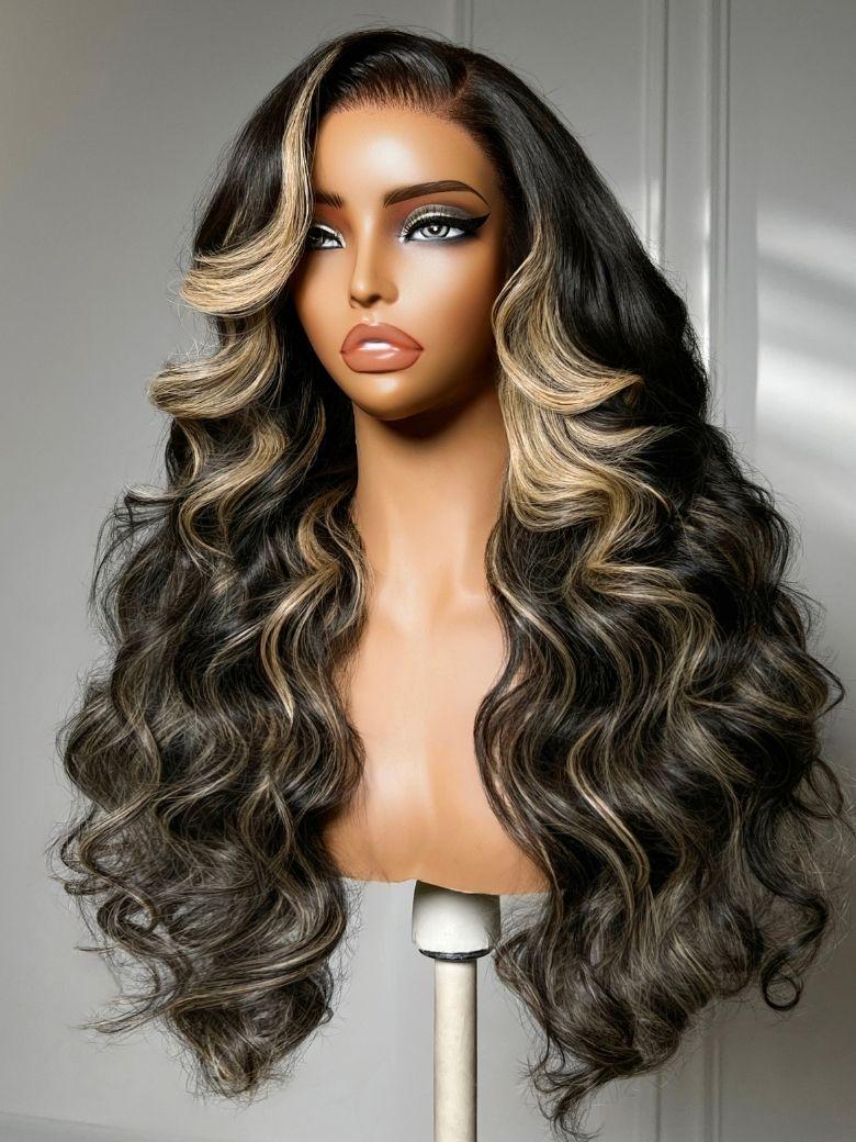 A model displays the UNice 7x5 Bye Bye Slip Lace Black With Blonde Face-Framing Highlights Body Wave Wig, showing a wig with long wavy hair and a brown and blonde color.