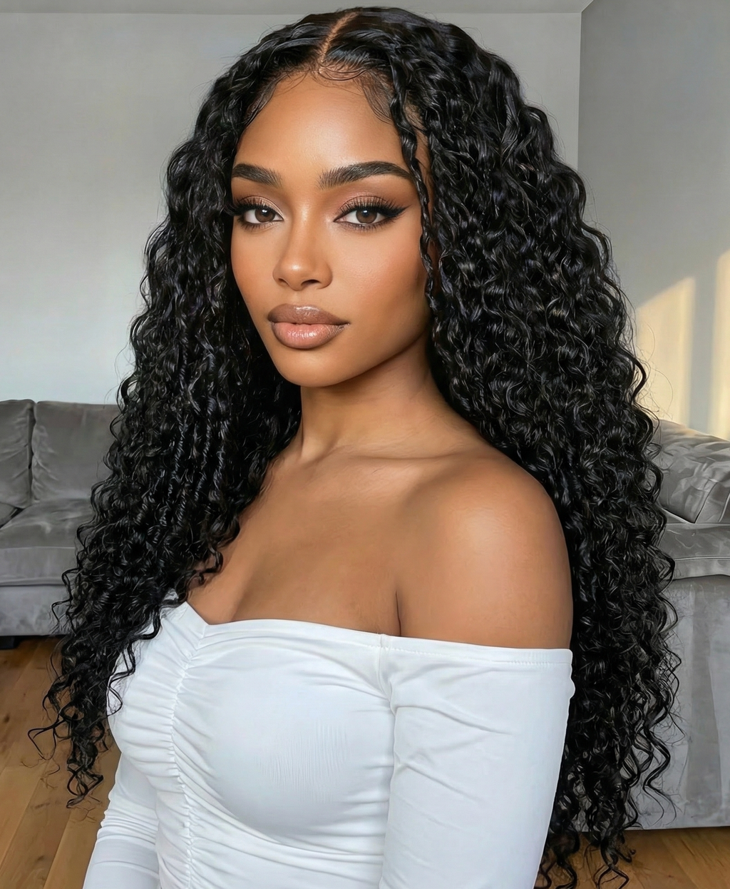 A model displays the UNice Bye Bye Slip 7x5 Lace Natural Black 4D Mixed Texture Burmese Curly Wig with, showing a model with long curly hair wearing a white top.