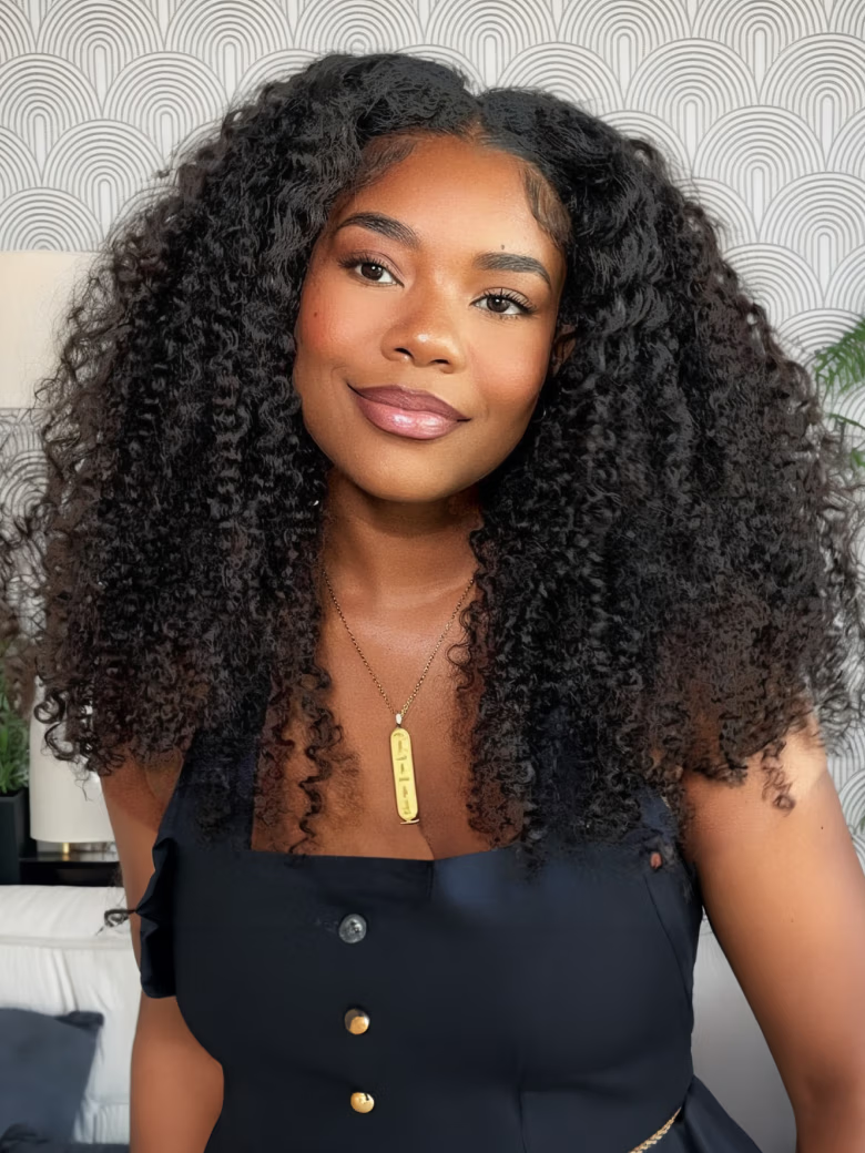 A model displays the UNice New V Part Kinky Curly Glueless 0 Skill Needed Wig, showing a model with long curly hair wearing a black dress and kinky curly texture, curly.