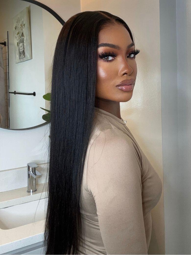 A model displays the UNice ByeBye Knots Wig 7x5 Glueless Lace Black Yaki Straight Wig With Elastic, showing a model with long black hair in a bathroom and straight.