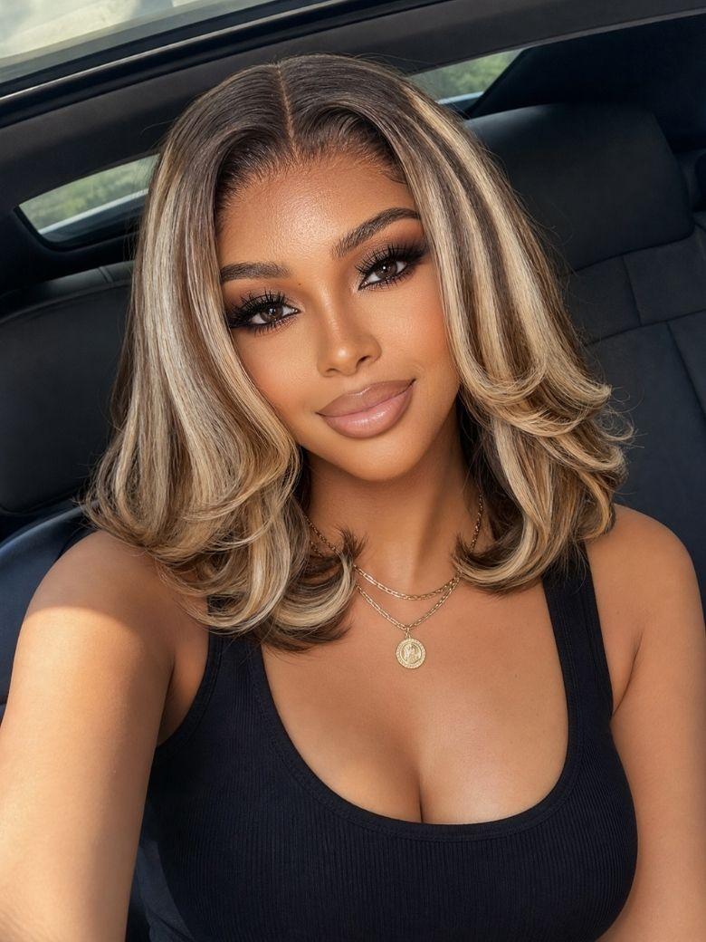 A model displays the UNice Bye Bye Slip 7x5 Lace Warm Brown with Beige Blonde Ribbon Highlights Layered wig, showing a model with blonde hair and a black top sitting.