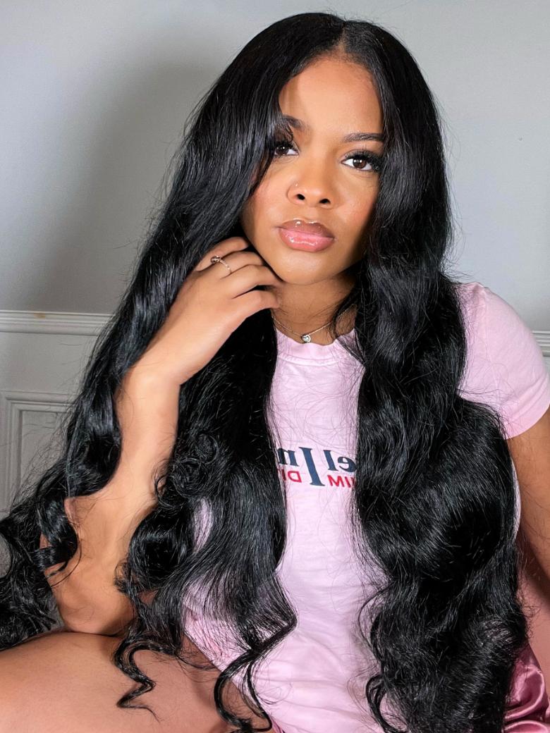 A model displays the UNice 22''= $89 Beginner Friendly V Part 150% Density Natural Black Body Wave Wig, showing a model with long black hair sitting on a bed and body.