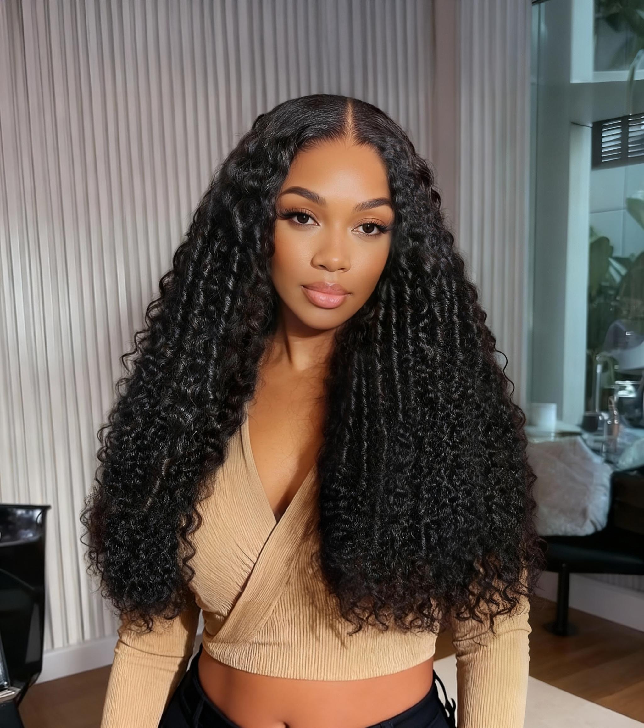 A model displays the UNice 18''-22'' UNice 7x5 Lace Bye Bye Knots Black Defined Coils 3C-4A Blend Curly wig, showing a model with long curly hair wearing a tan sweater.