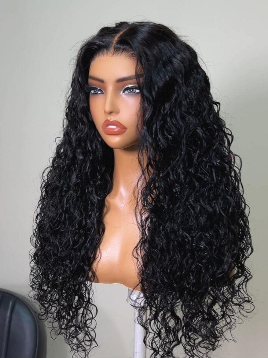 A model displays the UNice Bye Bye Slip 7x5 Lace Warm Brown with Beige Blonde Ribbon Highlights Layered wig, showing a model with blonde hair and a black top sitting.