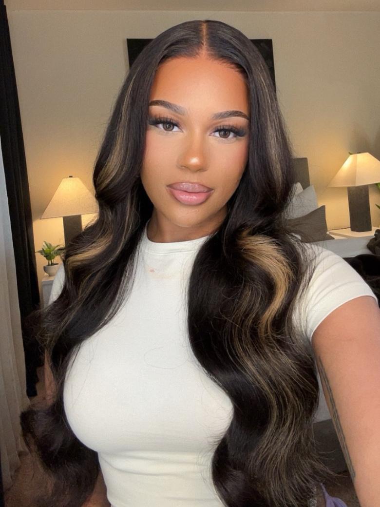 A model displays the UNice Bye Bye Knots Wig 7x5 Glueless Lace Black With Blonde Highlights 3D Body Wave, showing a model with long hair wearing a white top and body.