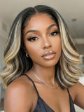 A model displays the UNice 7x5 Bye Bye Slip Lace Dark Brunette with Ash Blonde Highlight Layered Wavy Bob, showing a model with blonde hair and a black top.
