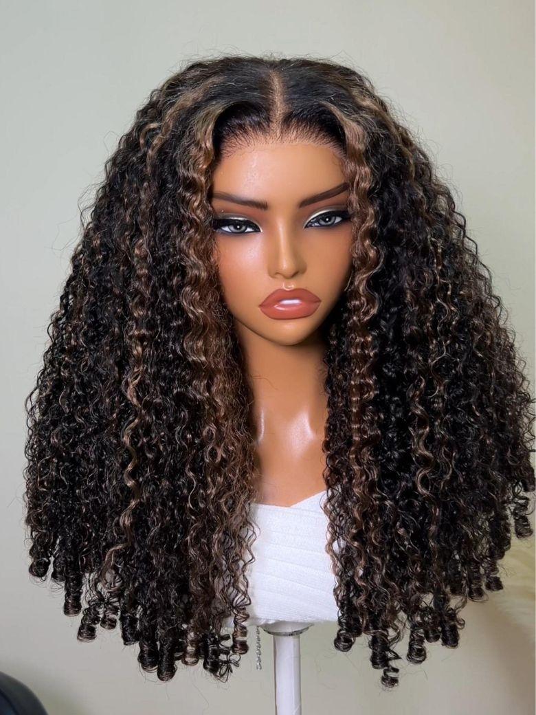 A model displays the UNice Bye Bye Slip 7x5 Lace Warm Brown with Beige Blonde Ribbon Highlights Layered wig, showing a model with blonde hair and a black top sitting.