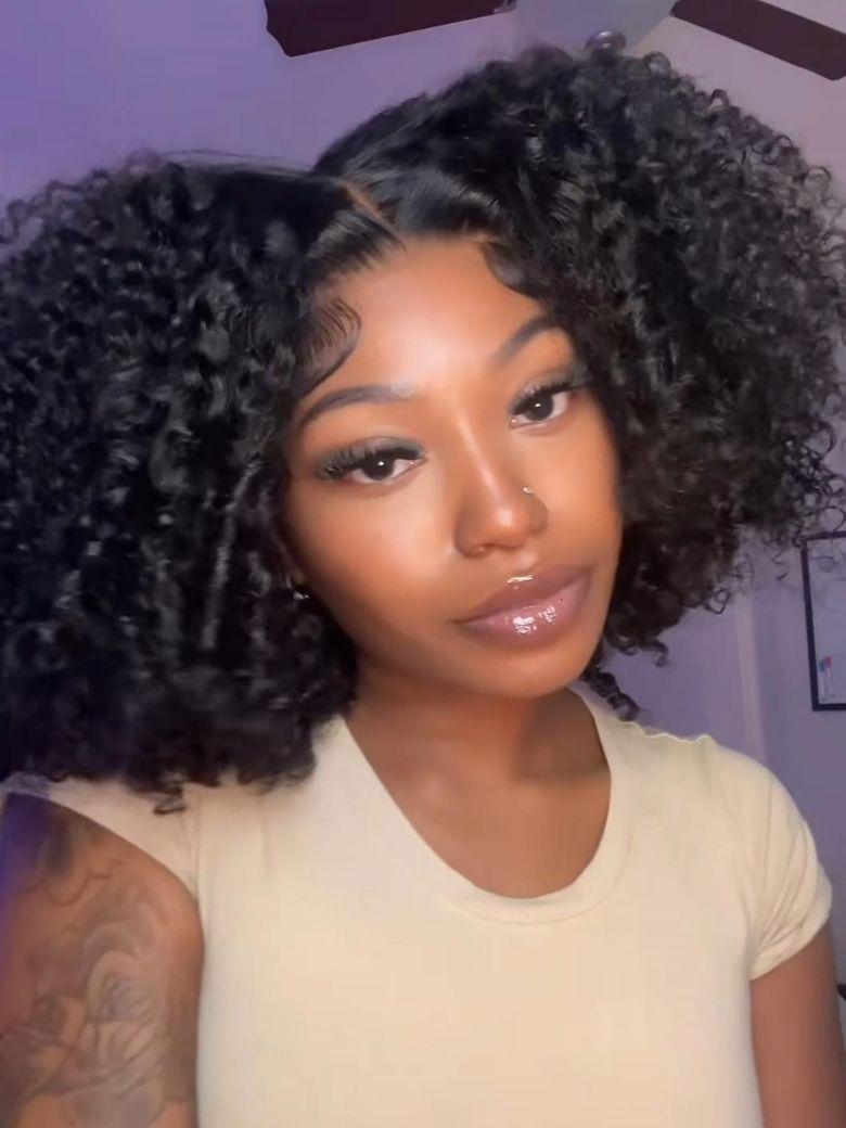 A model displays the UNice 7x5 Lace Bye Bye Slip Natural Black Afro Kinky Curly with Finger Coil Ends wig, showing a model with long curly hair and a white shirt.
