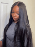 A model displays the UNice 7x5 Bye Bye Slip Yaki Straight Black Glueless Wig With Invisible Drawstring, showing a model with long black hair standing in front of a door.