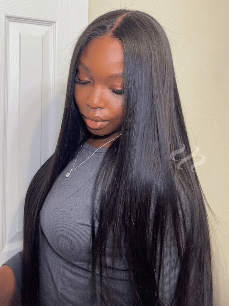 A model displays the UNice 7x5 Bye Bye Slip Yaki Straight Black Glueless Wig With Invisible Drawstring, showing a model with long black hair standing in front of a door.