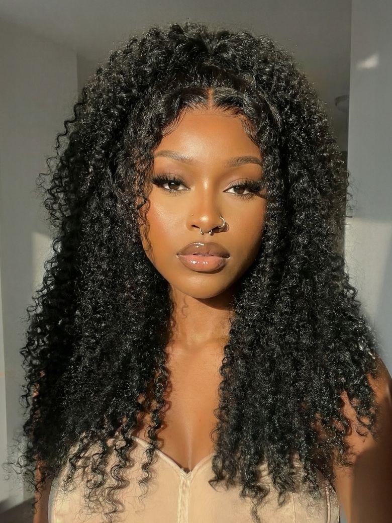 A model displays the UNice Invisi Drawstring 22" Bye Bye Knots 7x5 Lace Black Fluffy Kinky Coils Texture Wig, showing a model with long curly hair wearing a tan colored.